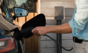 Person ansluter en elbil till en laddbox vid huset